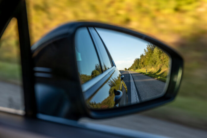 Car mirror view of country road. Travel with green landscapes.