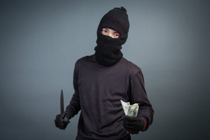 Criminals wear black mask and hold dark on gray background.