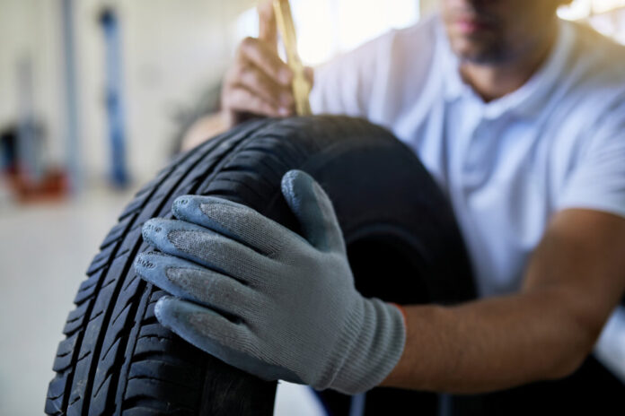 Close-up of repairman checking depth of car tire in a workshop.