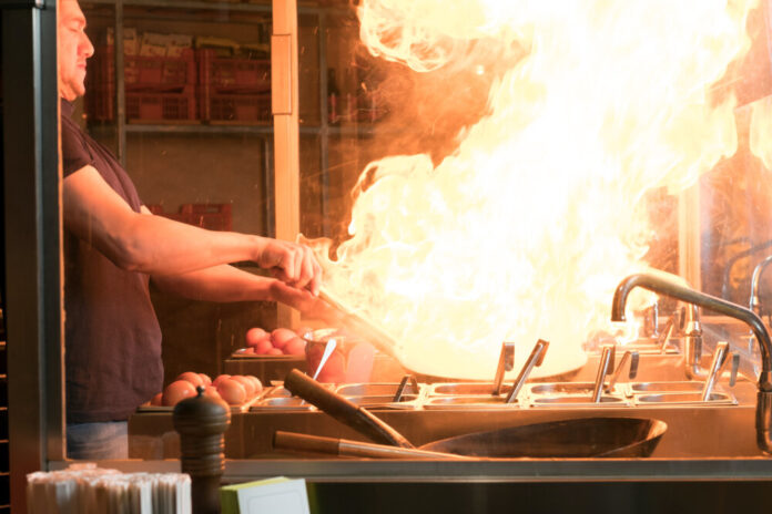 Cooking process in an Asian restaurant. Cook is fry vegetables with spices and sauce in a wok