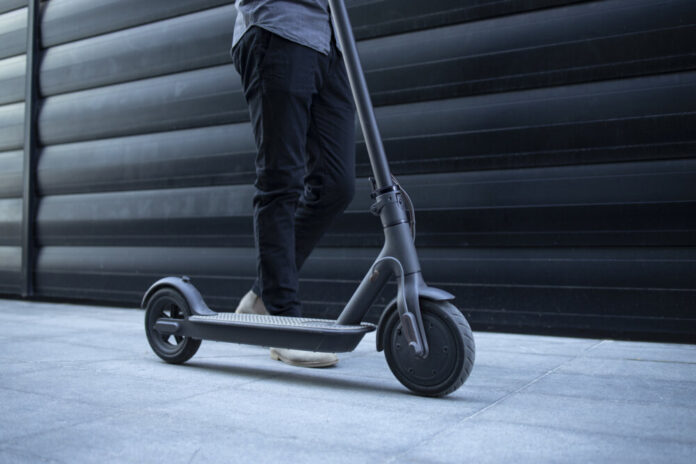 Unrecognizable modern person walking by his electric scooter.