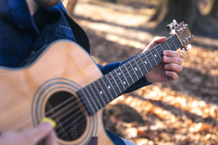 Close-up, a man plays an acoustic guitar in the autumn forest.
