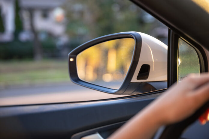Young woman driving a car. Hands on the wheel. Side mirror in the car.